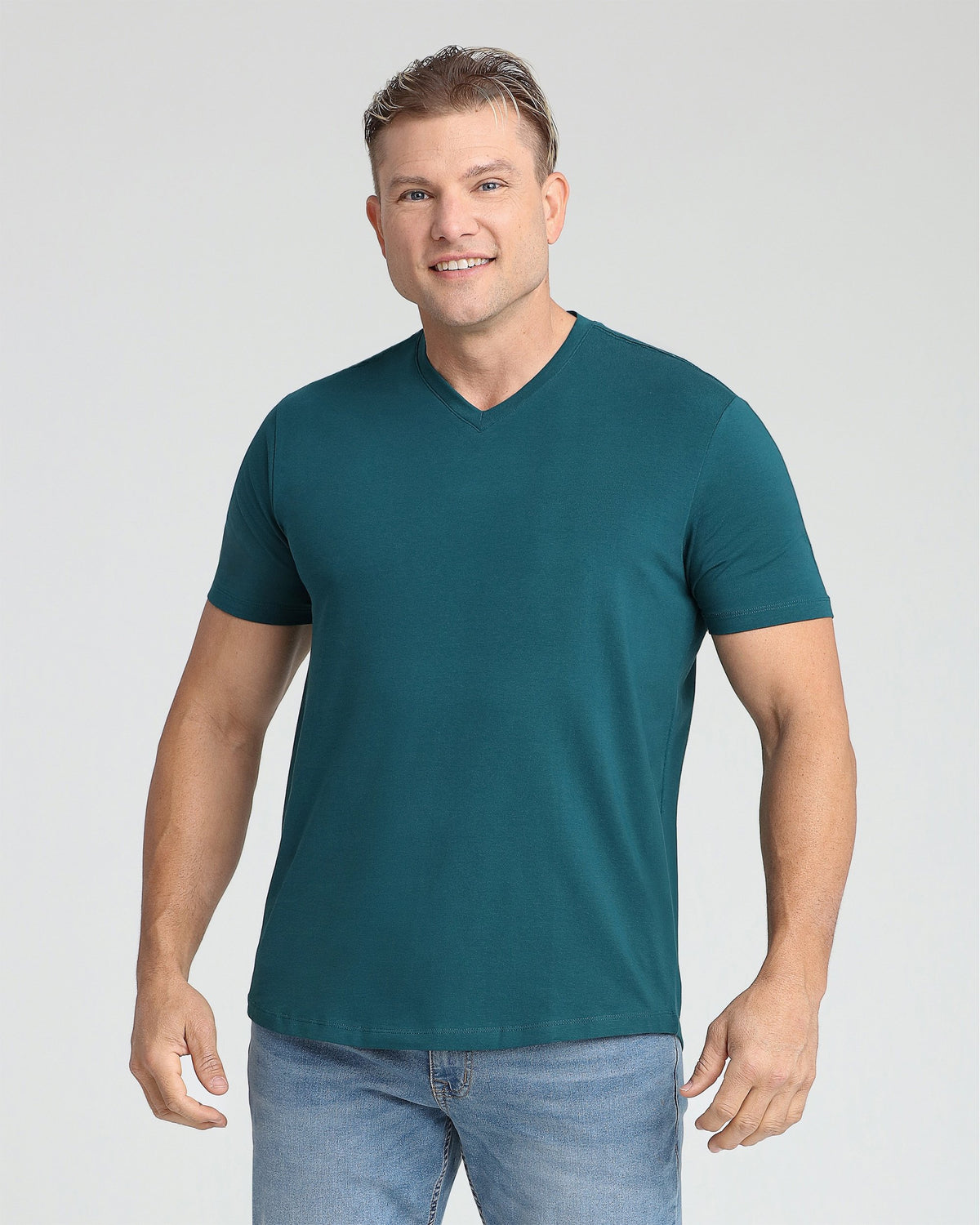 Man wearing teal v-neck t-shirt and light blue jeans against white background.