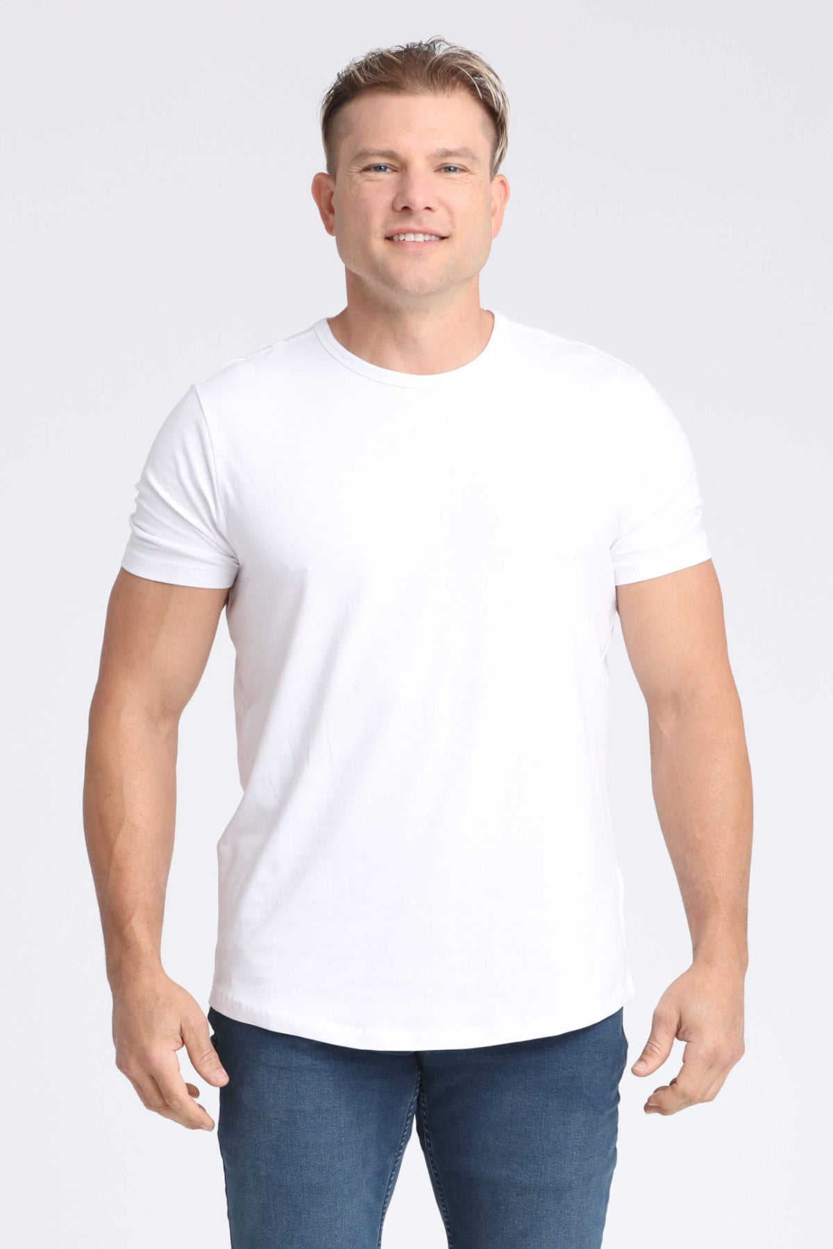 Man wearing a white crew neck t-shirt with short sleeves and dark blue jeans.