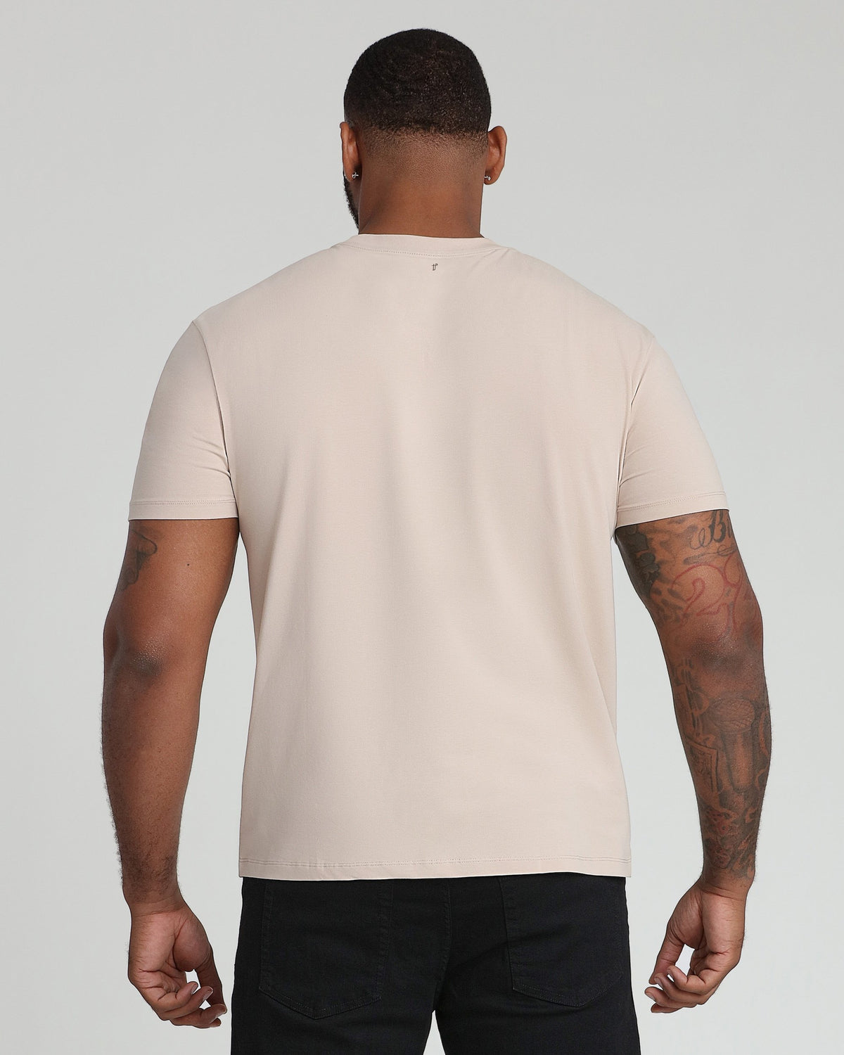 Tan crew neck t-shirt with short sleeves shown on a man wearing black pants, back view.