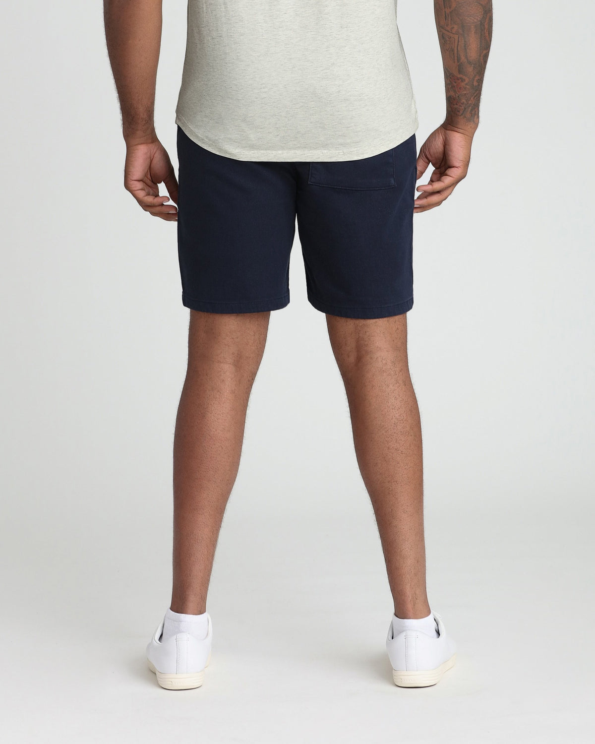 Man wearing navy athletic shorts with gray t-shirt and white socks, back view.