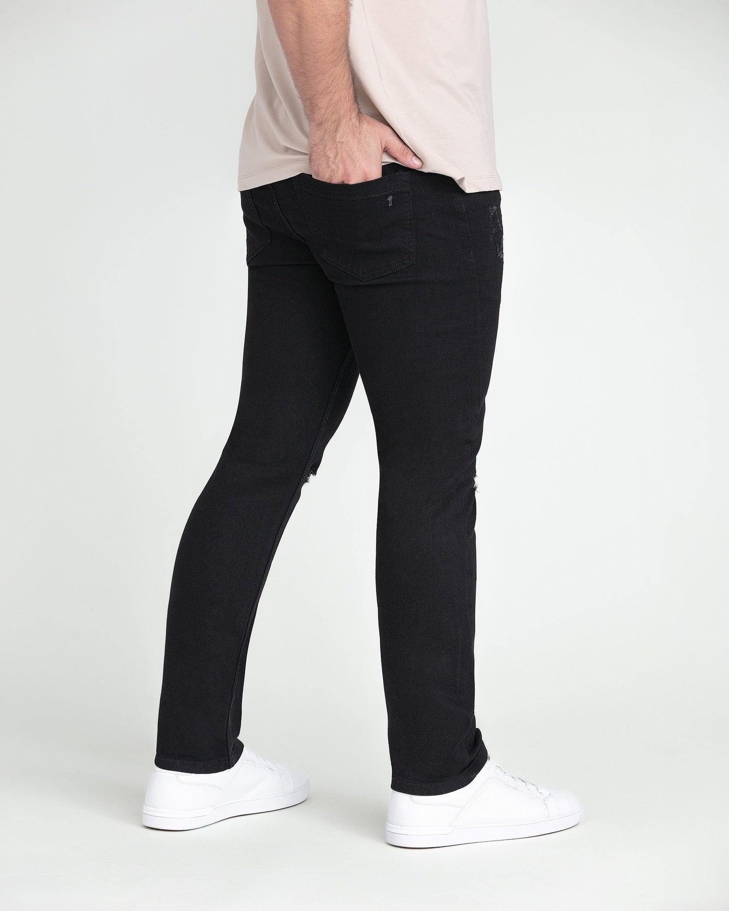 Black slim fit jeans with ripped thigh detail on model wearing white sneakers.