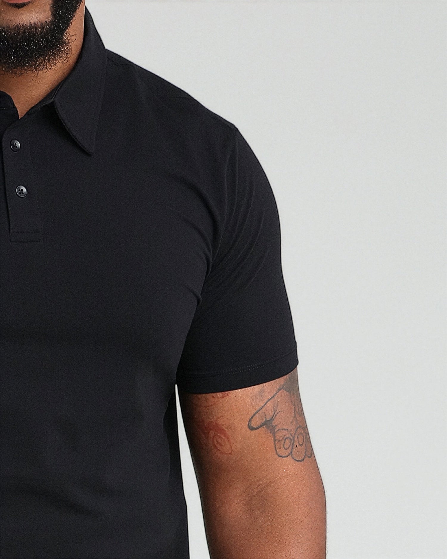 Black polo shirt with short sleeves and button front closure, shown on model.