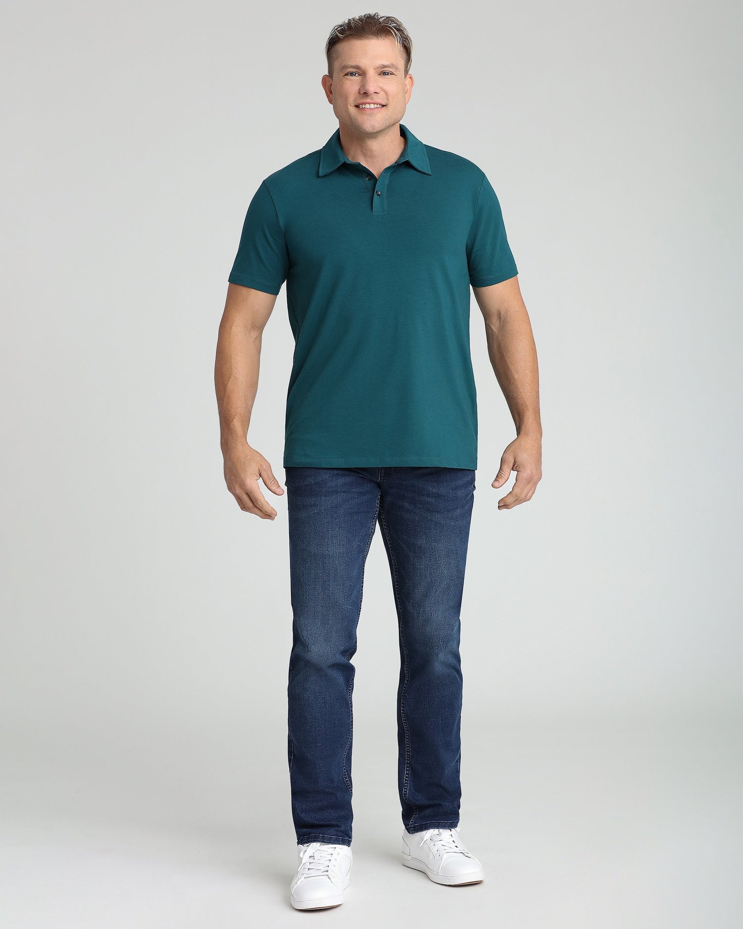 Man wearing teal short-sleeve polo shirt with dark jeans and white sneakers.