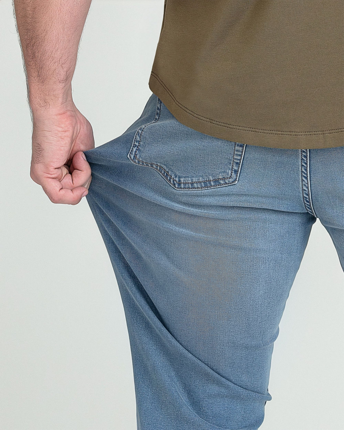 Light indigo jeans with curved back pockets and stitching detail, shown on model wearing olive shirt.