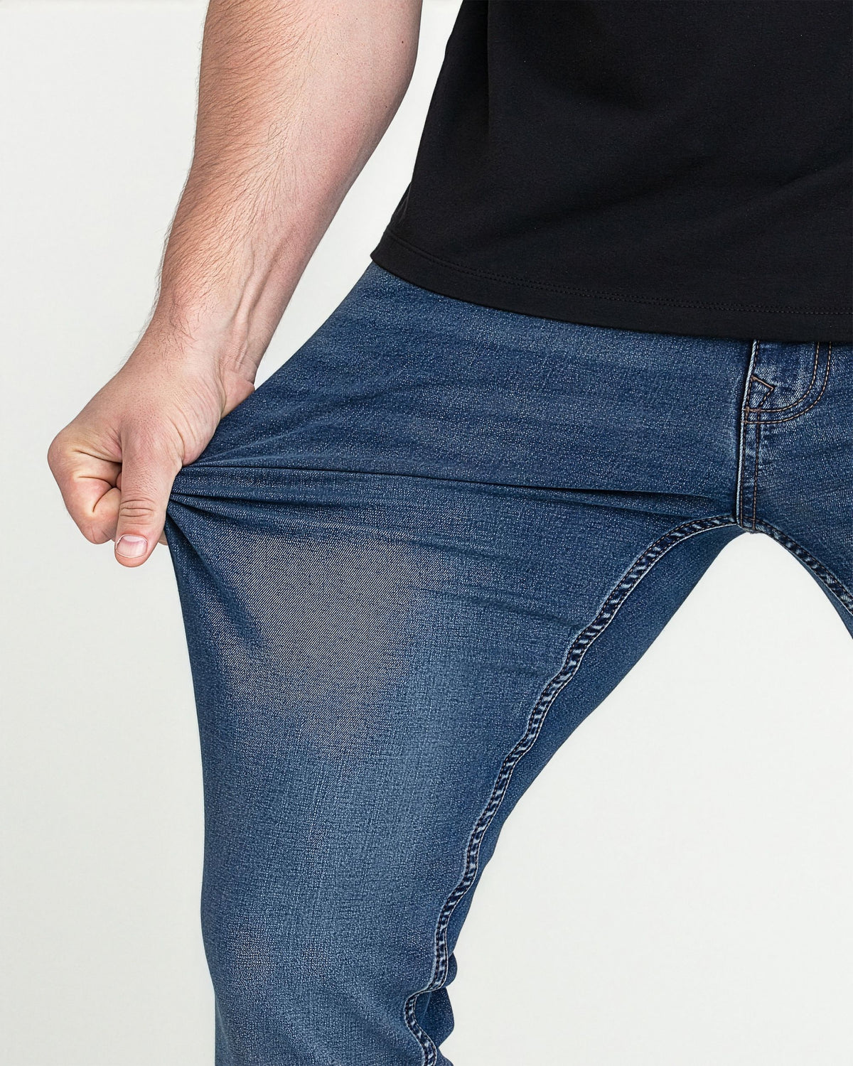 Man wearing medium blue slim fit jeans with black shirt, showing fit at thigh and waistband.