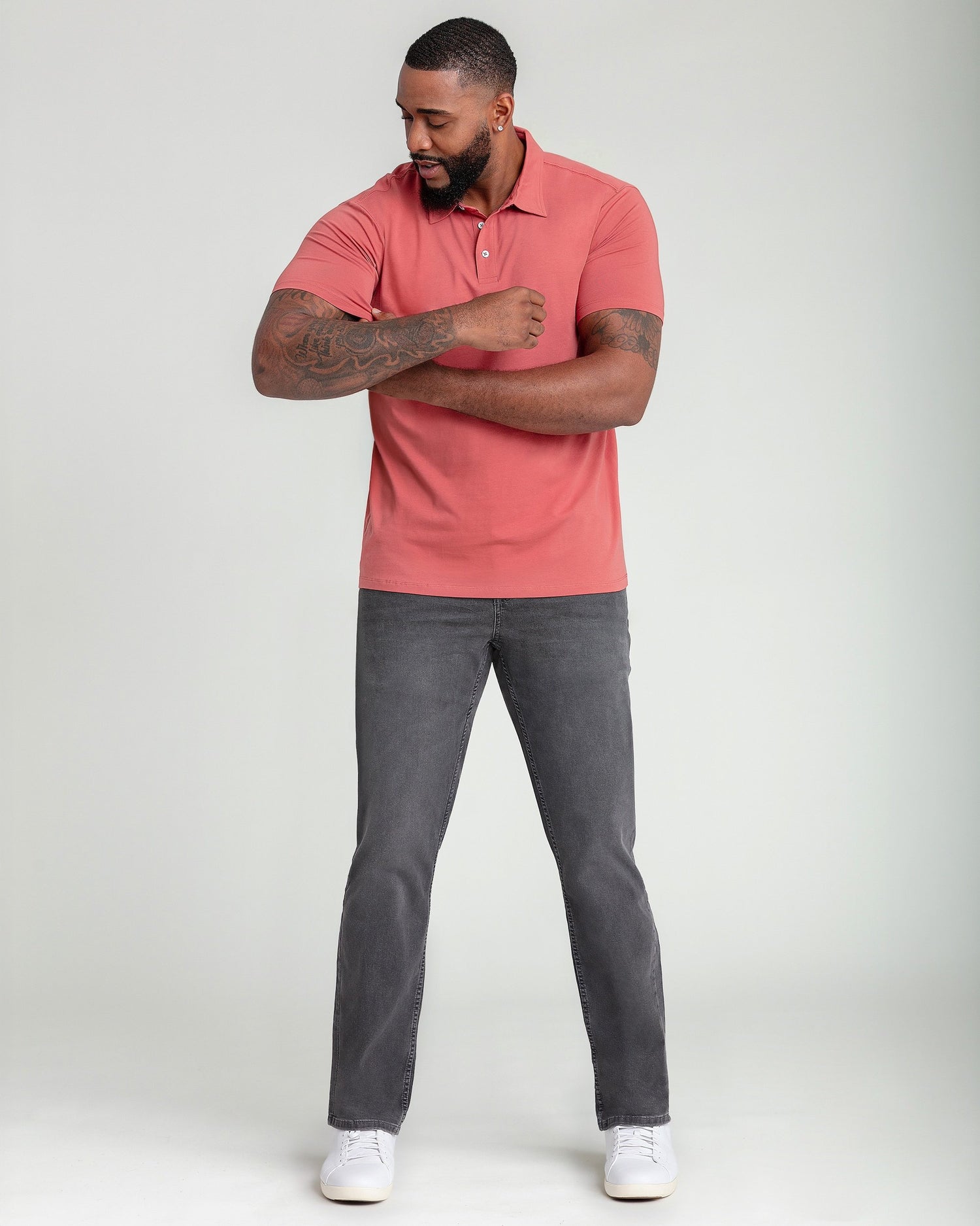 Man wearing nantucket red short-sleeve polo shirt with button placket and gray jeans.
