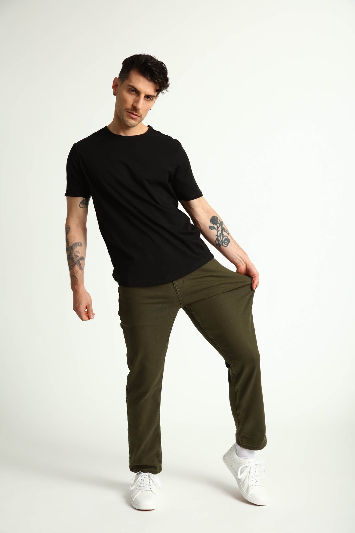 Man wearing black short-sleeve t-shirt and olive green slim fit pants with white sneakers.