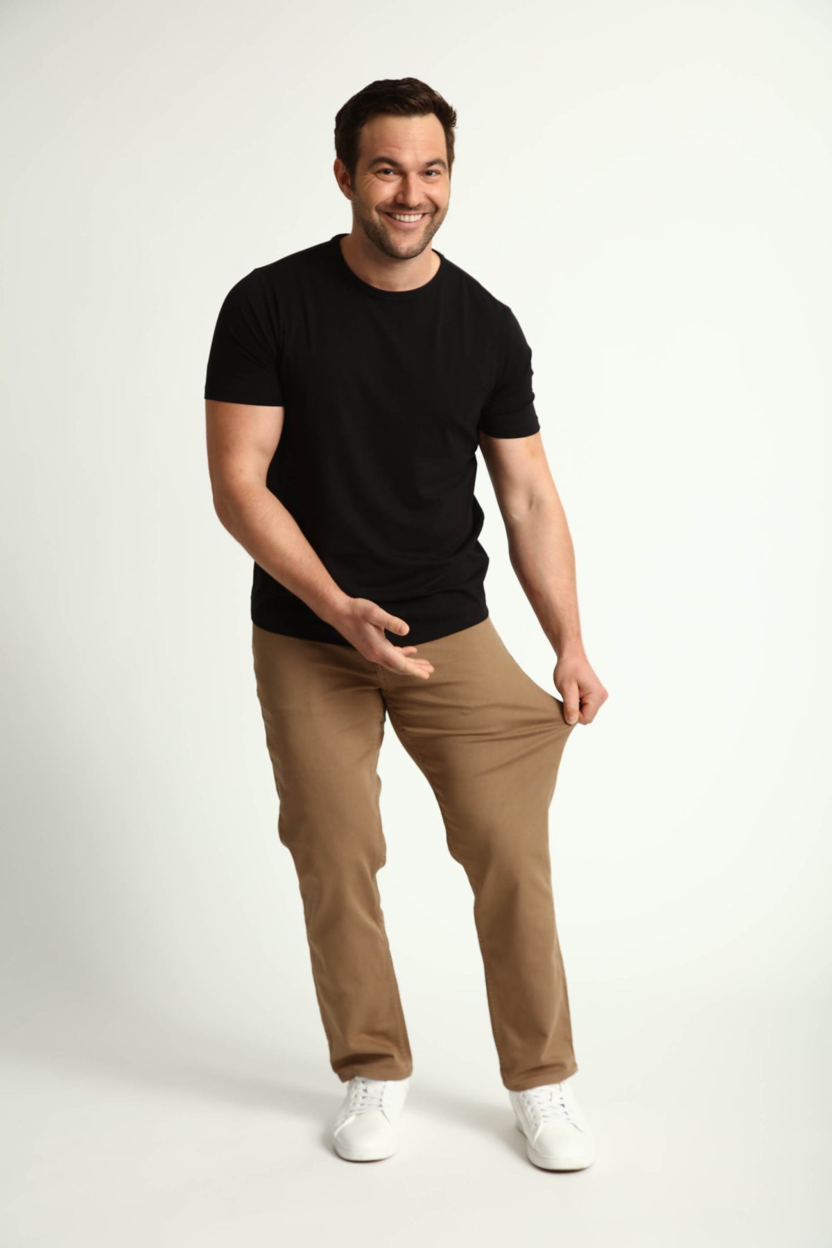 Man wearing black short-sleeve t-shirt and dark khaki athletic fit pants with white sneakers.