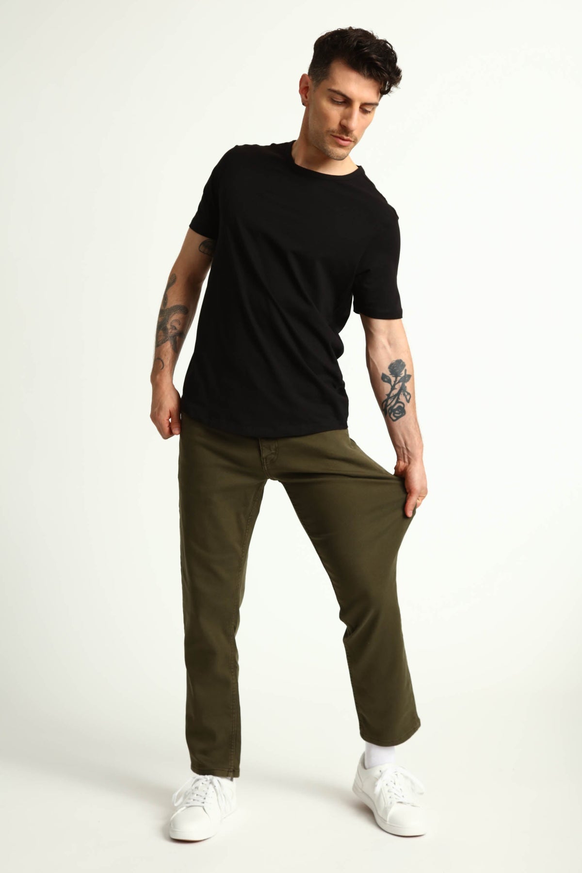Man wearing black short-sleeve t-shirt and olive green athletic fit pants with white sneakers.