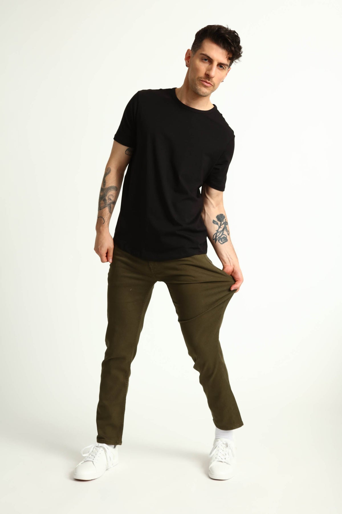Man wearing black short-sleeve t-shirt and olive green slim-fit pants with white sneakers.