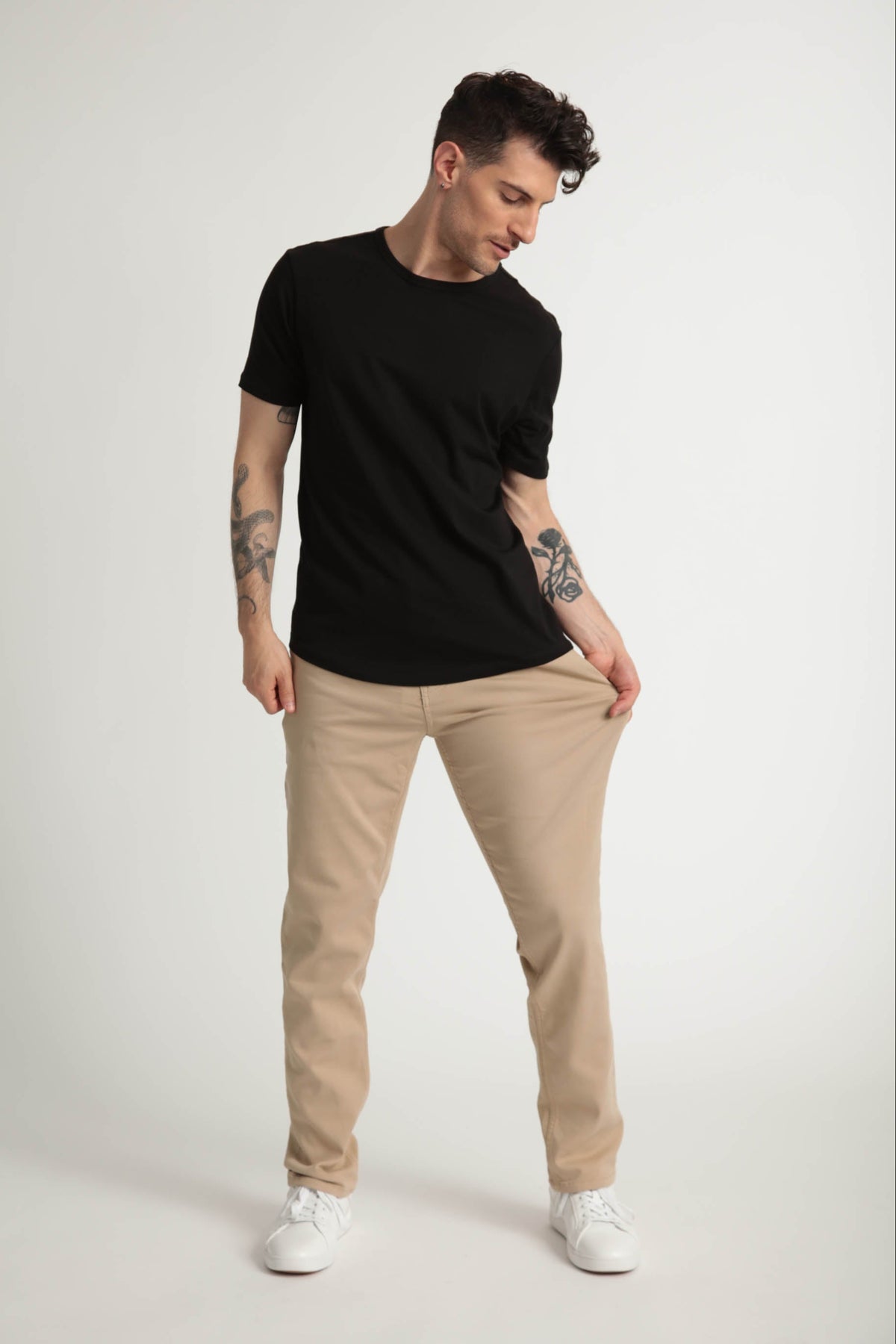 Man wearing black short-sleeve t-shirt and light khaki slim fit pants with white sneakers.