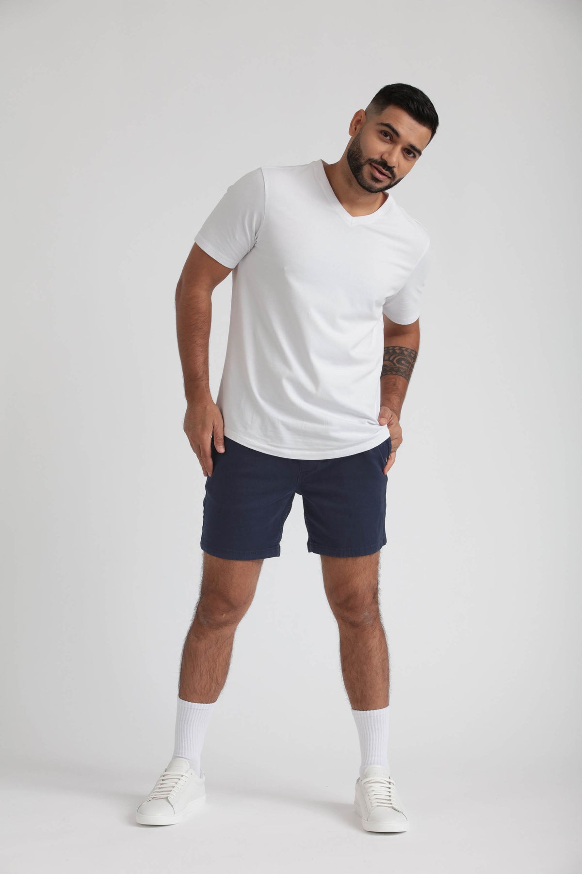 Man wearing white t-shirt and navy slim fit shorts with white socks and sneakers.