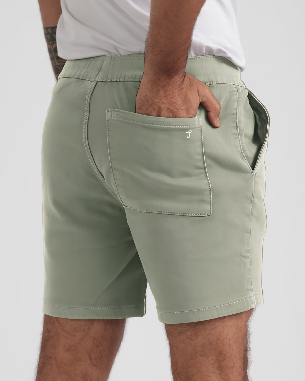 Sage green athletic fit shorts with elastic waistband and back patch pocket, worn with white t-shirt.