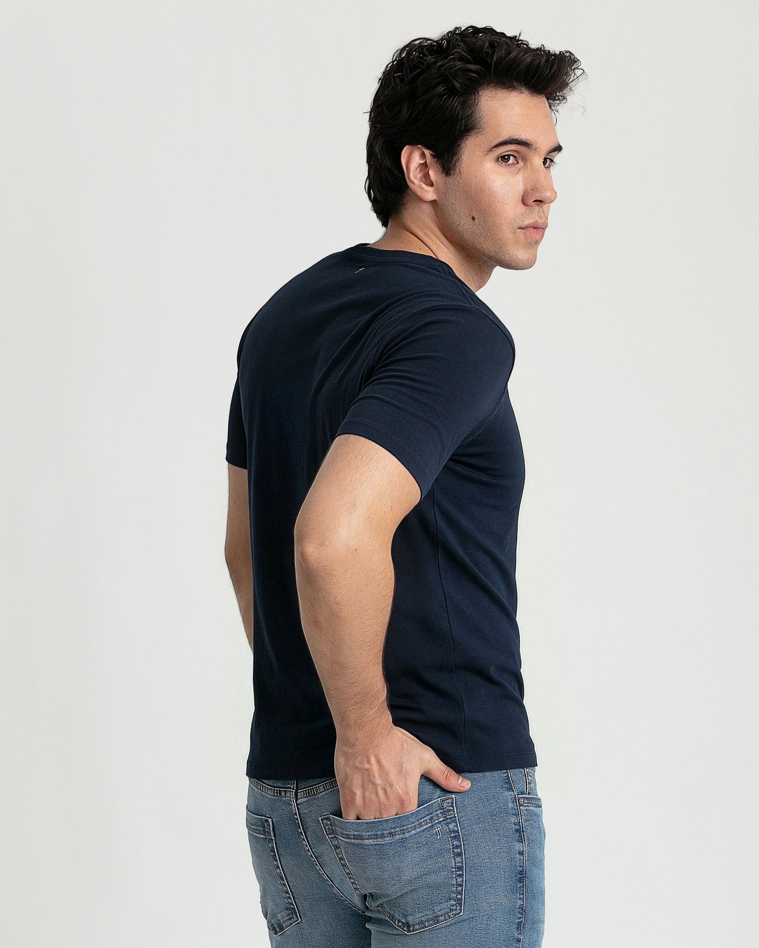Man wearing navy blue v-neck t-shirt and light blue jeans, shown from side angle.