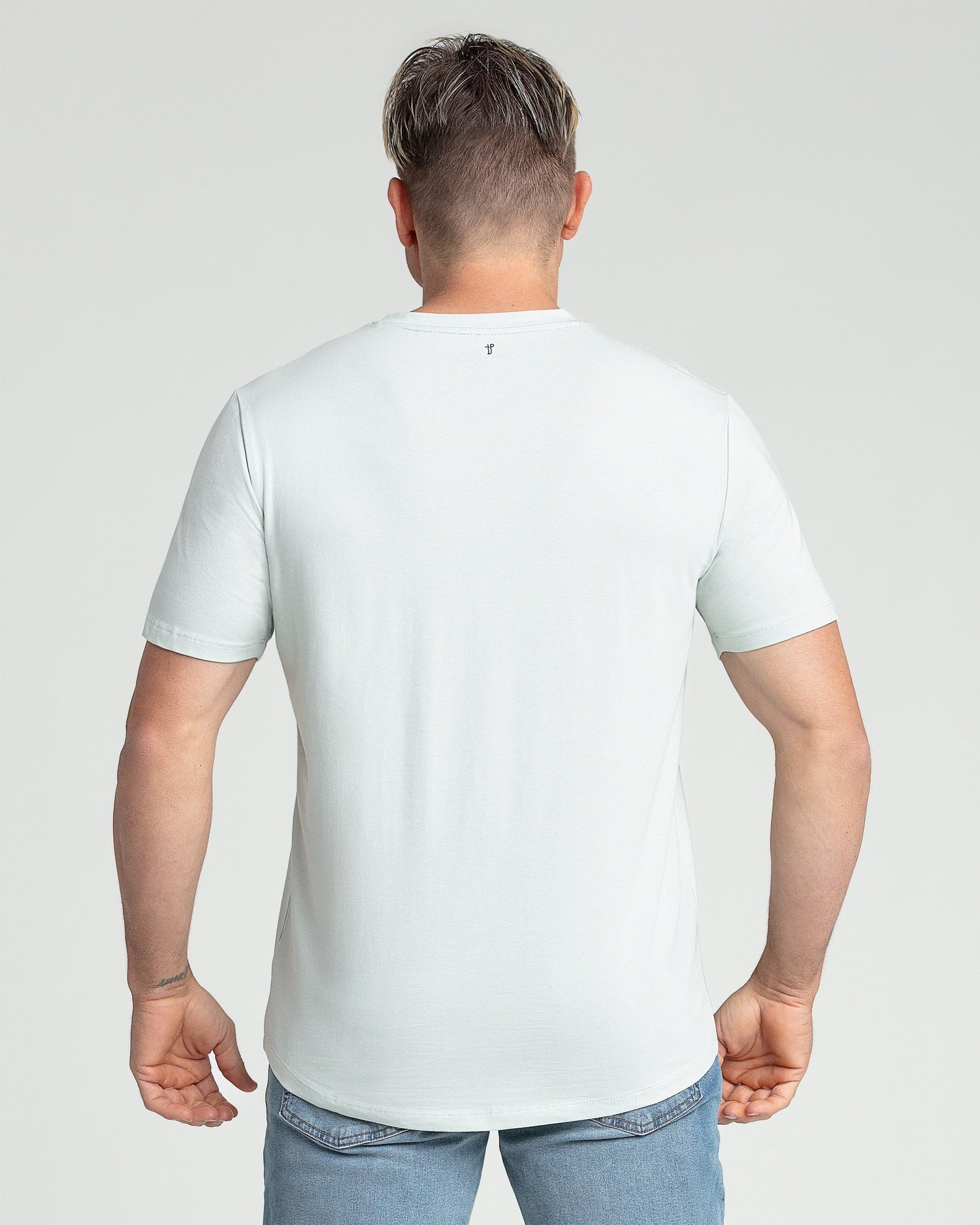 Man wearing white V-neck short-sleeve t-shirt and blue jeans, shown from back view.