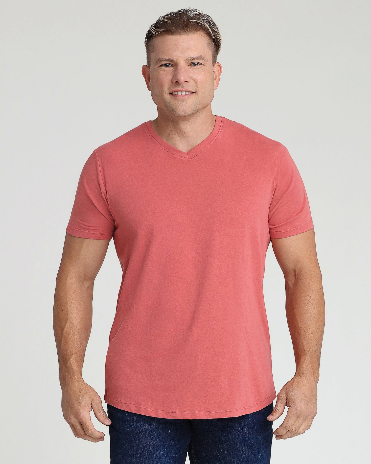 Man wearing coral-pink v-neck t-shirt with short sleeves and dark jeans.