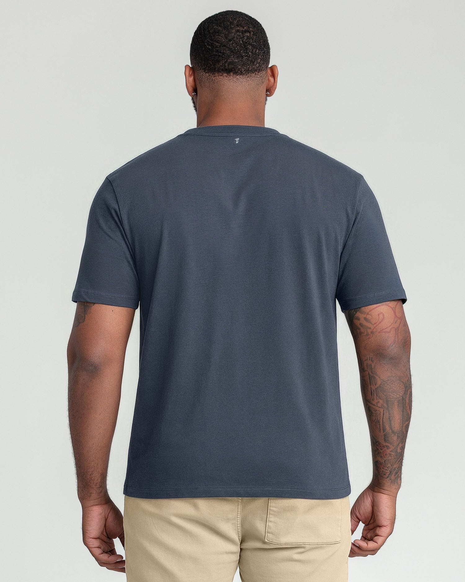 Man wearing dark blue crew neck t-shirt and beige pants, shown from back.