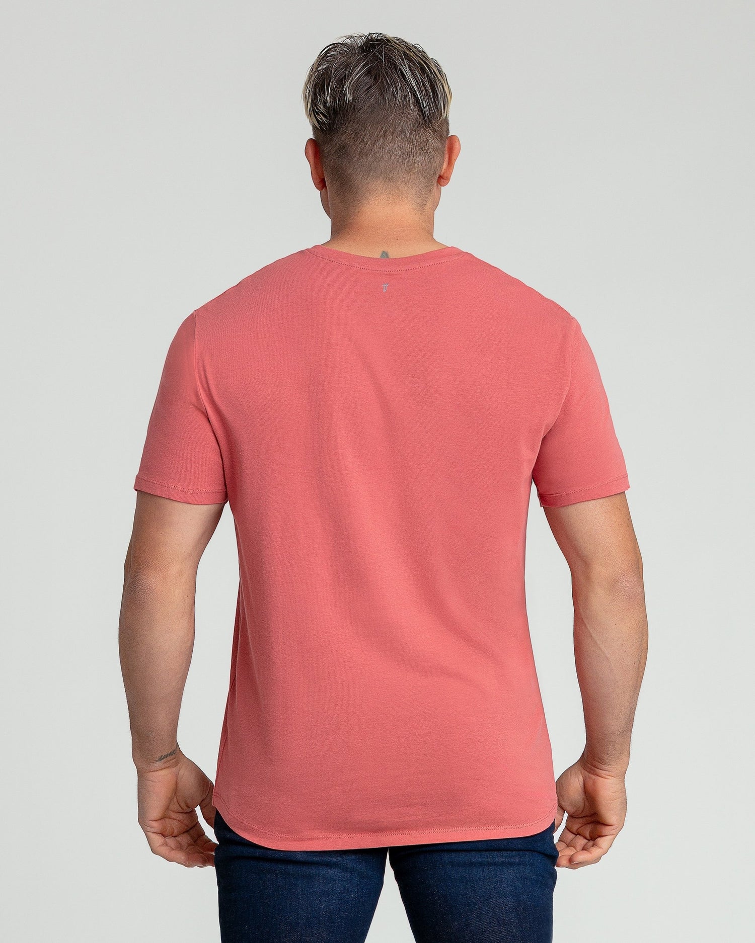 Man wearing coral-pink v-neck t-shirt and dark jeans, shown from back.
