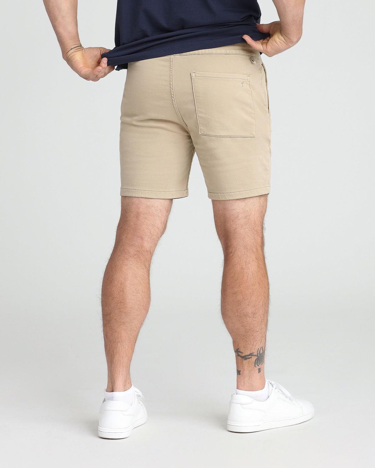 Light khaki slim fit shorts with back pocket detail, worn with navy shirt and white sneakers.
