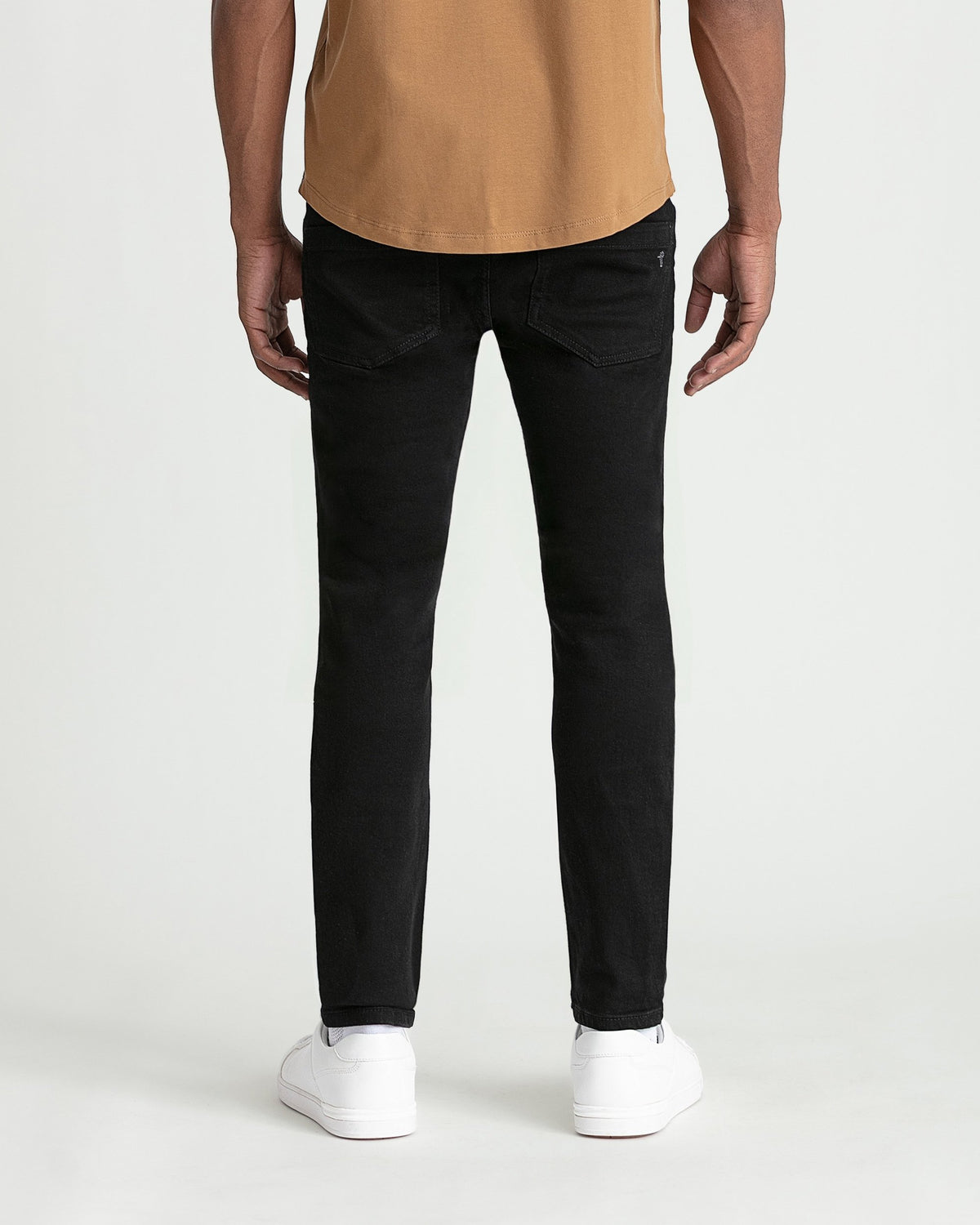 Black skinny fit jeans on male model wearing tan shirt and white sneakers.