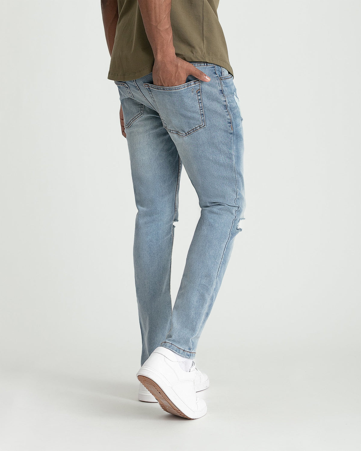 Light blue skinny fit jeans with ripped knee detail and frayed hem on model wearing white sneakers.