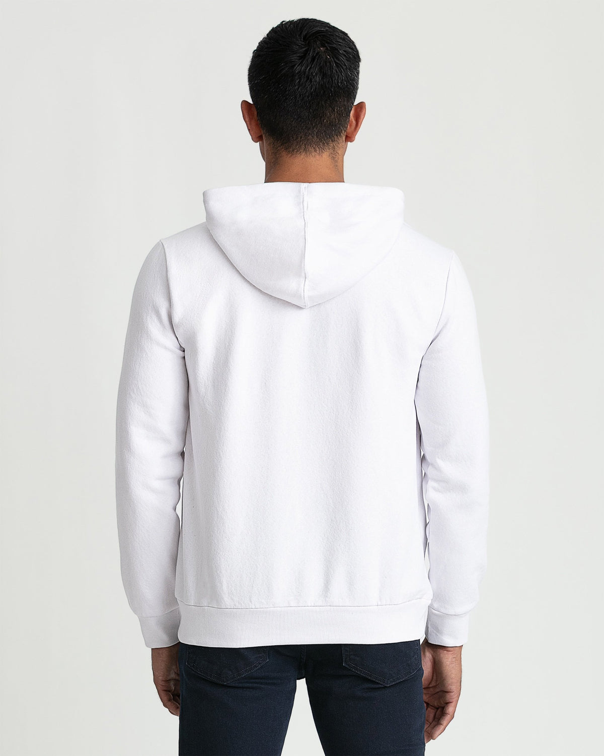 White pullover hoodie with kangaroo pocket and drawstring, shown from back on male model wearing dark jeans.