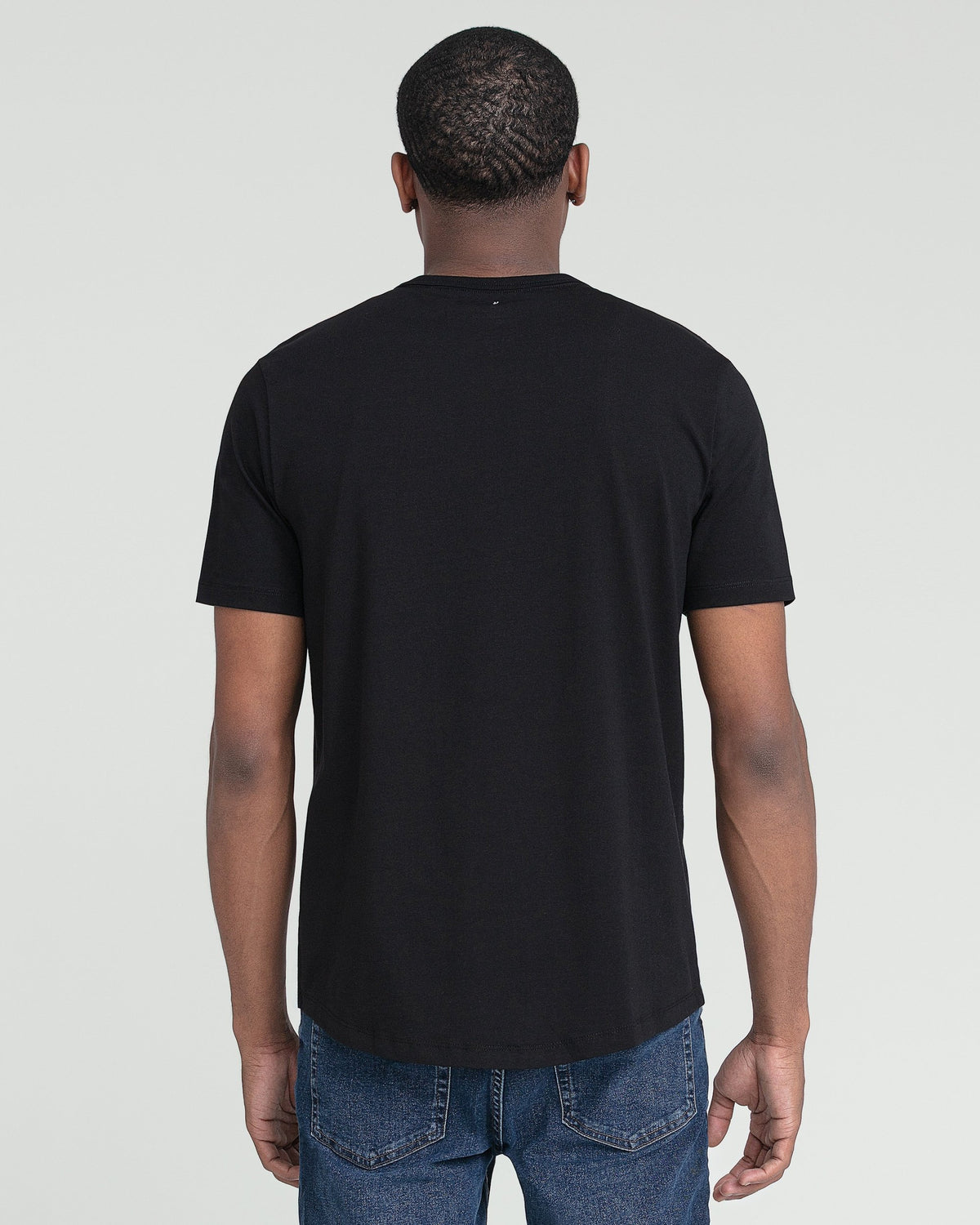 Black crew neck t-shirt shown from back on male model wearing blue jeans.