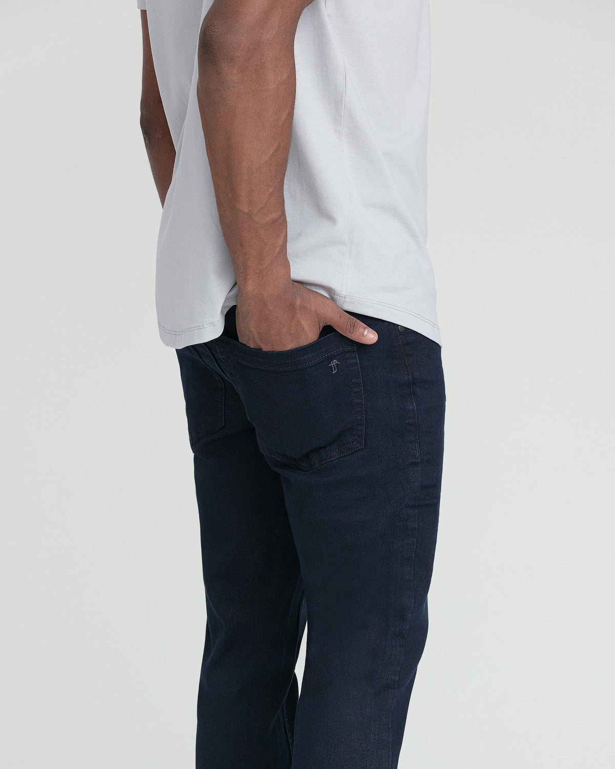 Man wearing white t-shirt and dark blue slim fit jeans with back pocket detail.