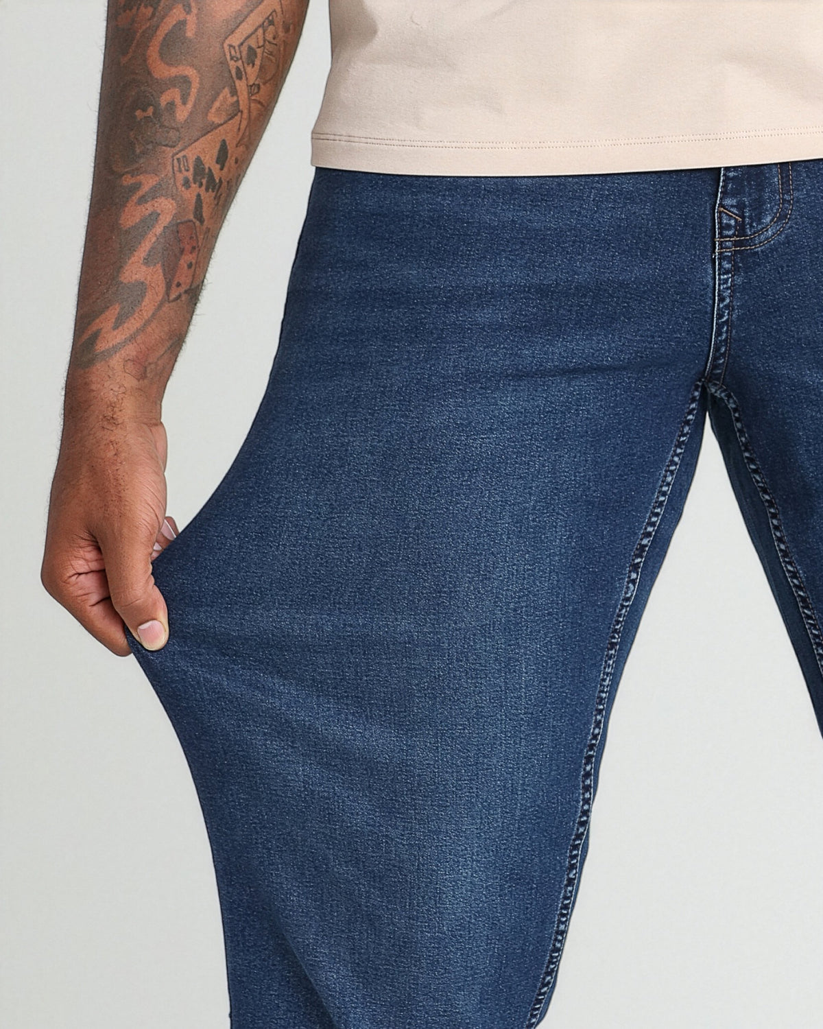 Man wearing dark blue denim jeans with cream t-shirt, showing thigh and waistband detail.