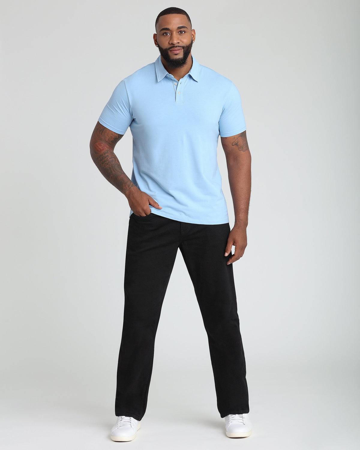Man wearing light blue short-sleeve polo shirt with collar and button placket, paired with black pants and white sneakers.