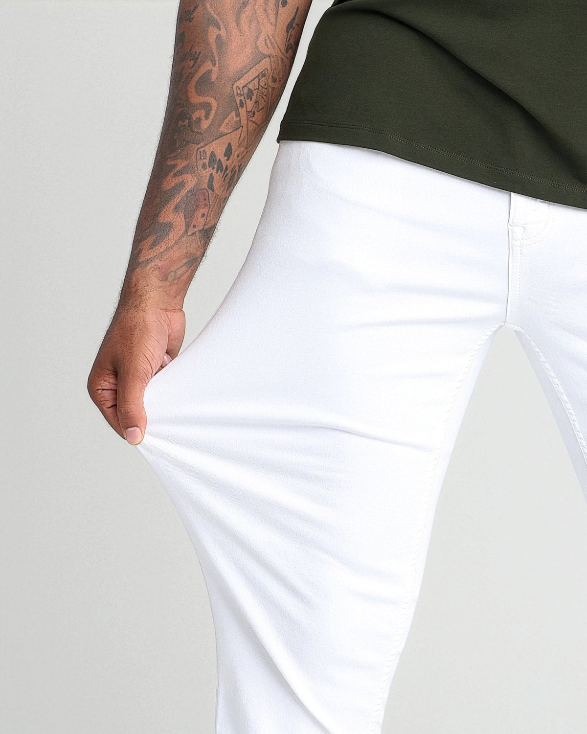 White athletic fit pants with tapered leg, shown on model wearing olive green shirt.