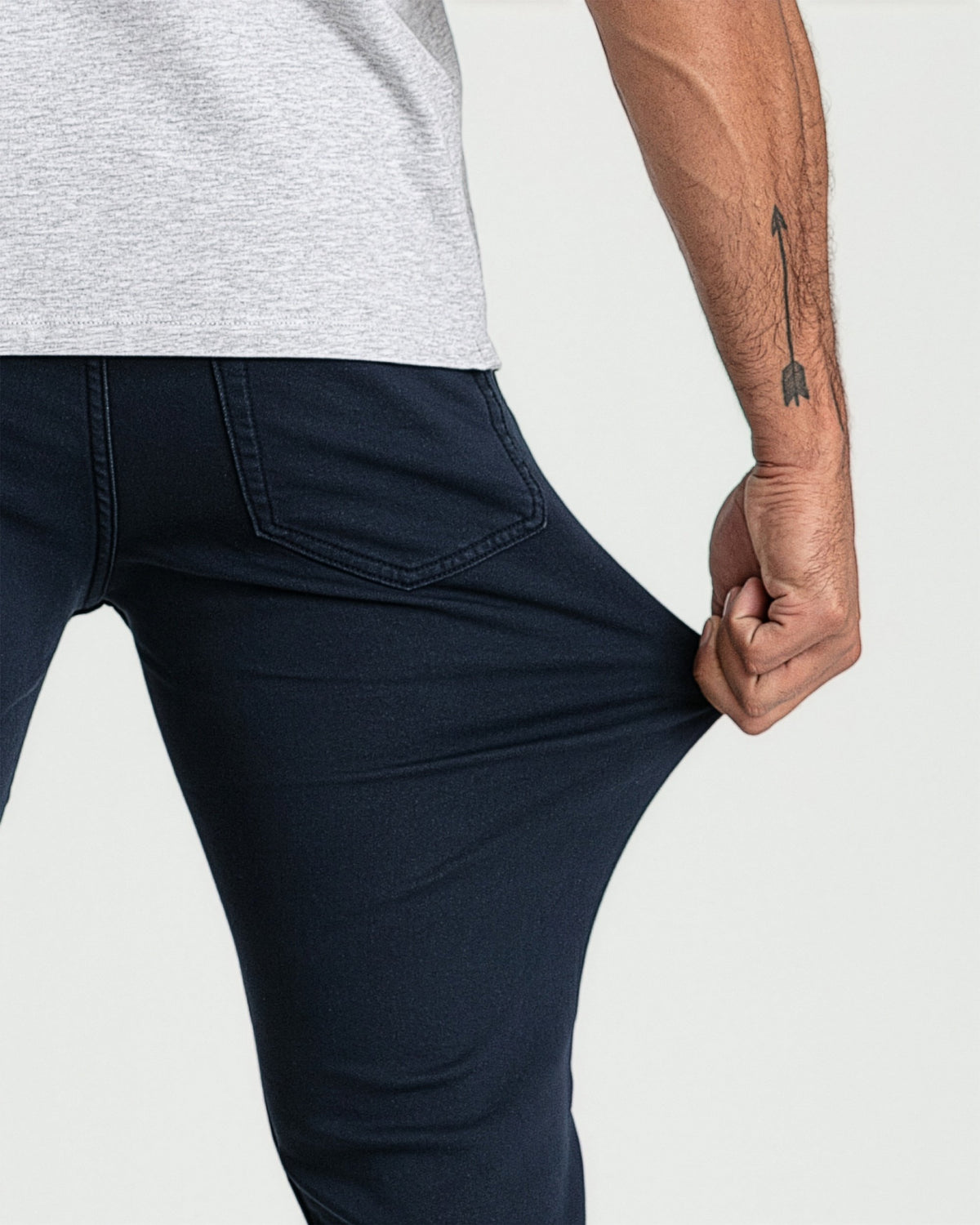 Man wearing light gray t-shirt and navy slim-fit jeans with back pocket detail.