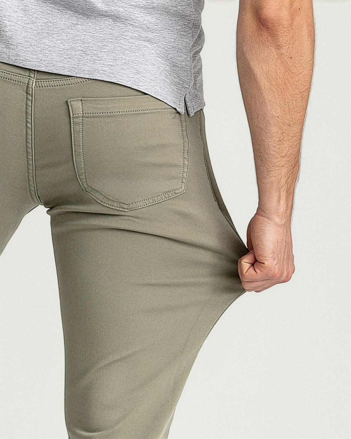 Man wearing light gray t-shirt and sage green slim fit pants with back pocket detail.