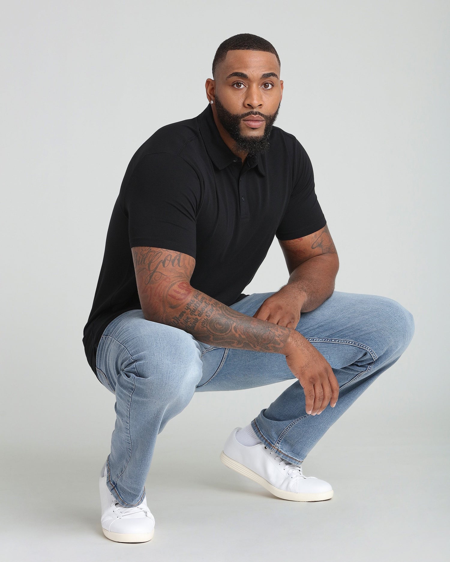 Black polo shirt with short sleeves and collar, worn with light blue jeans.