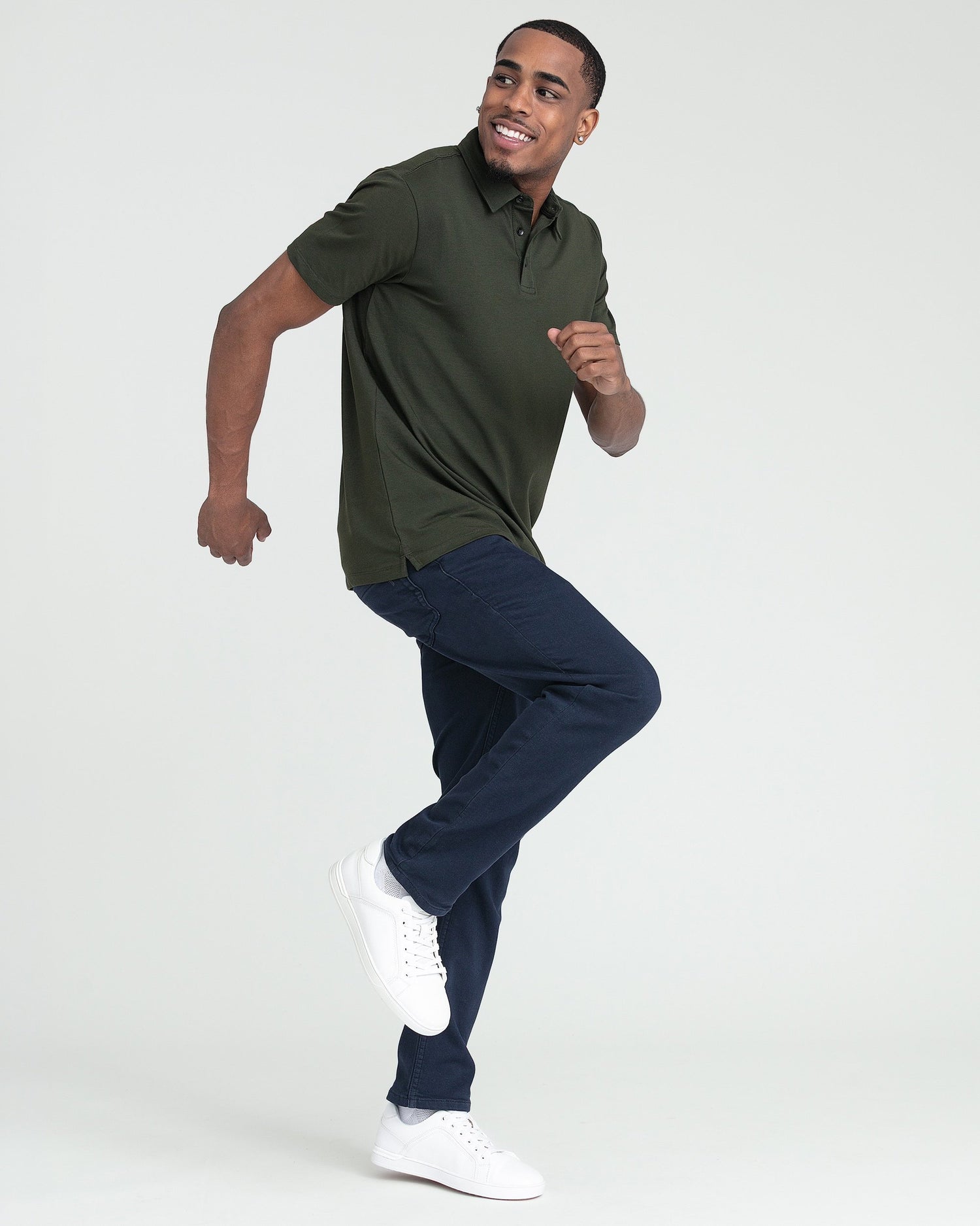 Man wearing olive green polo shirt with dark navy jeans and white sneakers.