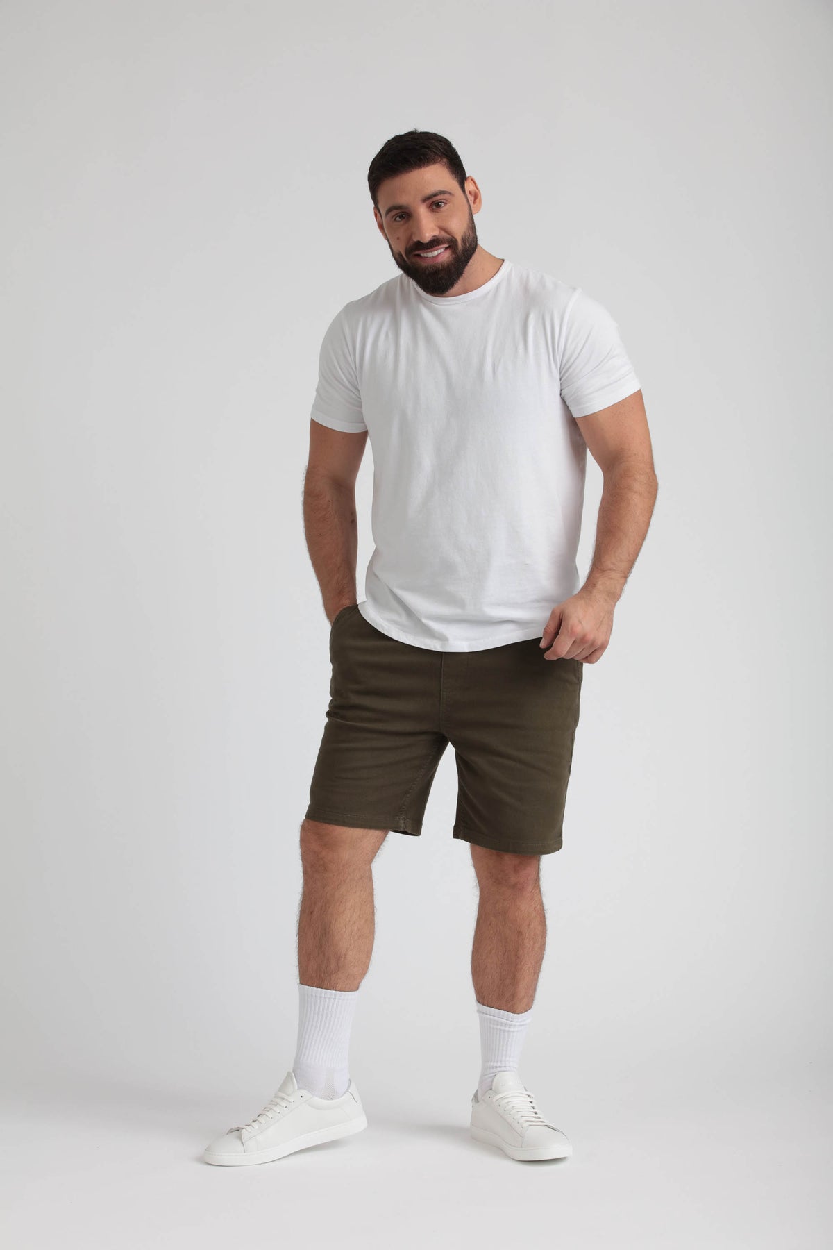 Man wearing white t-shirt and olive green athletic shorts with white socks and white sneakers.