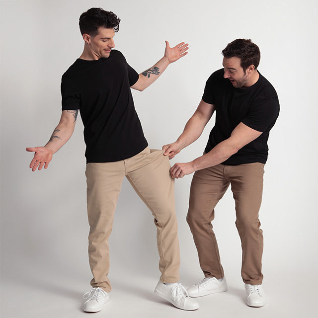 Two men wearing black shirts and beige pants on a plain background