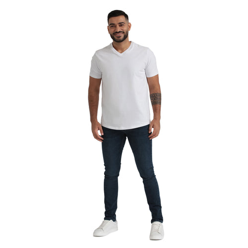 Man wearing white v-neck t-shirt and dark blue skinny fit jeans with white sneakers.